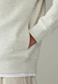 Lysegrå sweatshirt med et struktureret hørmønster, ribbede manchetter og en sidelomme med blød stoffinish.