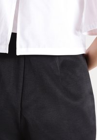 Biała bluzka z krótkim rękawem o prostym kroju, zestawiona z czarnymi spodniami o wysokim stanie z fakturowanego materiału, wyposażonymi w boczne kieszenie.