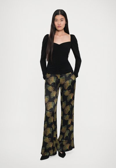 Top negru cu mâneci lungi, cu decolteu pătrată și detalii plisate; pantaloni largi cu un model de frunze verzi și portocalii pe un fond negru.