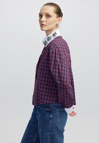 Camicia a quadretti in navy e rosso con colletto bianco decorato. Maniche lunghe, vestibilità rilassata e tessuto testurizzato.