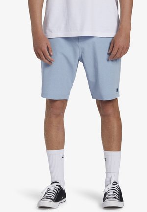 Light blue shorts made of a textured fabric, knee-length with a small logo patch on the hem, paired with black sneakers and white socks.