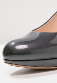 Pompe en cuir verni gris avec un bout arrondi, surface lisse et brillante, et intérieur beige, affichant un design épuré et élancé.