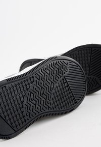 Suelas de zapatillas de goma negras con patrones texturizados, incluyendo diseños hexagonales y en zigzag, que demuestran funcionalidad de agarre y durabilidad.