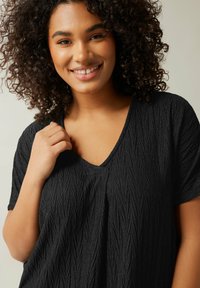 Schwarzes V-Neck-Top mit strukturiertem Design und vertikalen Falten, kurzen Ärmeln und lockerer Passform. Der Stoff ist leicht und weich.