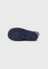 Semelle de chaussure en caoutchouc bleu marine, dotée d'un motif de grip texturé avec des formes circulaires et rectangulaires, ainsi qu'un logo surélevé sur le talon.