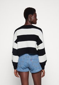 Svart-hvitt stripete strikkegenser med cropped design og vide ermer, kombinert med lyseblå denimshorts med oppbrett.