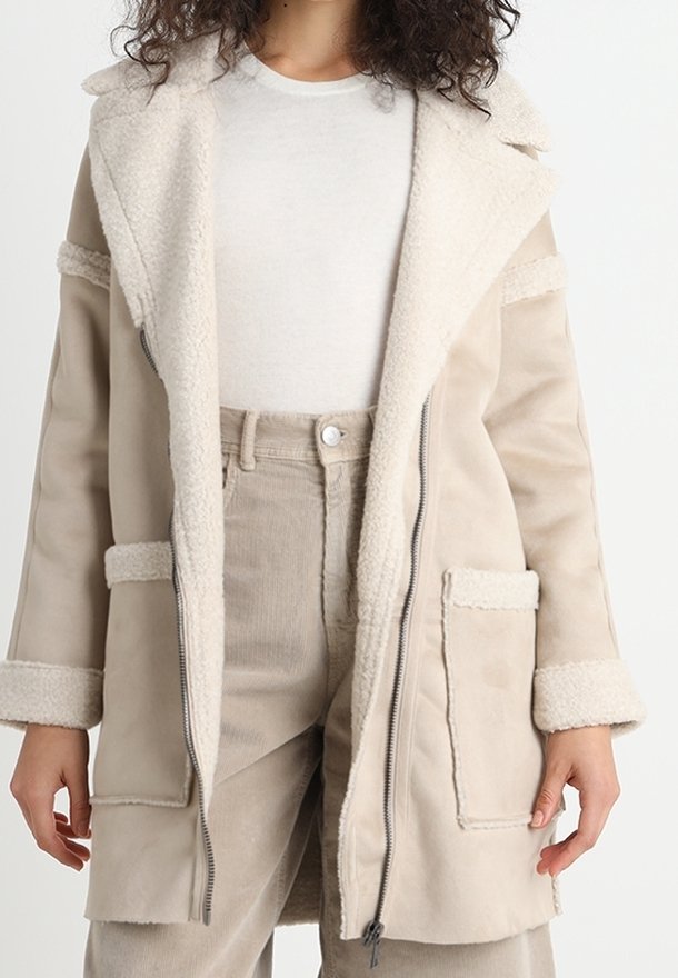 Chaqueta beige con cuello forrado de borreguito, cierre de cremallera en la parte delantera, dos bolsillos delanteros y tejido texturizado. Presenta un corte relajado y mangas largas.