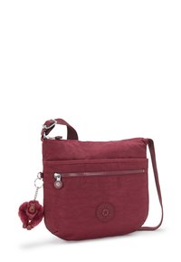 Burgundy crossbody bag made from soft fabric, features a front zipper pocket and a monkey keychain. Includes a long adjustable strap.