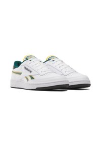 Sapatilhas brancas com detalhes em verde e amarelo, parte superior em pele lisa, detalhes perfurados, atacadores e sola em borracha. Logótipo da Reebok em destaque.