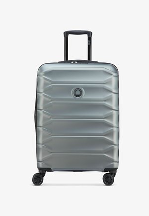 Valise rigide argentée avec surface texturée, quatre roues pivotantes et une poignée télescopique noire déployée.