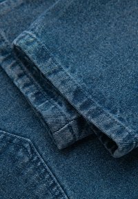 Tejido de mezclilla azul oscuro, doblado con detalles de costura visibles. Superficie texturizada con un ligero brillo, mostrando un acabado suave y un patrón clásico.