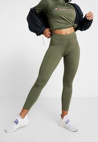 Olivgrünes Activewear-Set bestehend aus einem Cropped-Top und hochschneidigen Leggings, gefertigt aus glattem Stoff mit einem gestickten Logo-Detail.