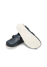Marineblaue Clogs mit glänzendem Finish, ausgestattet mit einem einzelnen Riemen und einer strukturierten weißen Außensohle. Hergestellt aus strapazierfähigem Material, mit einem weichen Innenfutter.