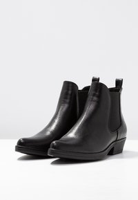 Bottines noires avec une texture lisse et polie, des panneaux latéraux élastiques et un petit talon empilé. Bout rond et détails minimaux.