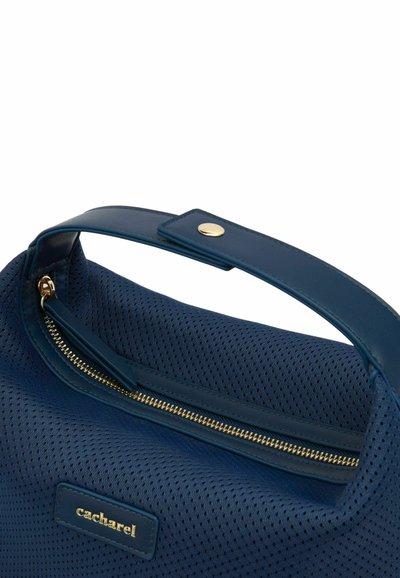 Navy blauwe handtas van geperforeerd materiaal, met een gouden ritsluiting en een platte handle. Merkenlabel zichtbaar aan de zijkant.
