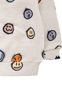 Sweatshirt bianco con vari volti sorridenti e espressioni colorate, con polsini a coste e un'etichetta dettagliata in basso.
