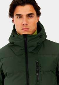 Zielona ocieplana kurtka z wysokim kołnierzem, zamkiem błyskawicznym z przodu oraz kieszenią na piersi. Posiada matową fakturę oraz regulowany kaptur z troczkami.