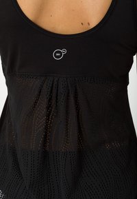 Top deportivo sin mangas negro que presenta una parte superior lisa y una sección inferior texturizada y perforada con una costura fruncida y detalle de marca.