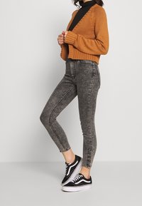 Suéter corto de punto naranja combinado con jeans de mezclilla negros de cintura alta y zapatillas negras, que cuentan con detalles en blanco y una textura desgastada.