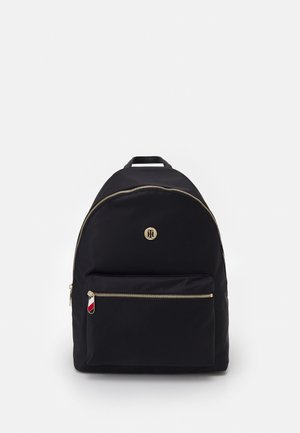 Schwarzer Rucksack mit Frontreißverschlusstasche, Reißverschlüssen in Goldoptik und kleinem rundem goldfarbenem Logo auf der oberen Vorderseite.