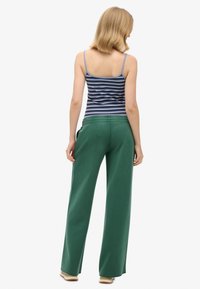 Zielone szerokie spodnie z elastycznym paskiem w talii, zestawione z niebieską i białą paskowaną bluzką na ramiączkach. Ubranie jest casualowe i wygodne.