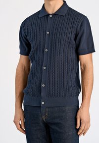 Granatowy, krótki sweter na guziki z teksturowanym wzorem warkocza, pięcioma guzikami z przodu oraz prążkowanymi mankietami i dołem, wykonany z miękkiego materiału.