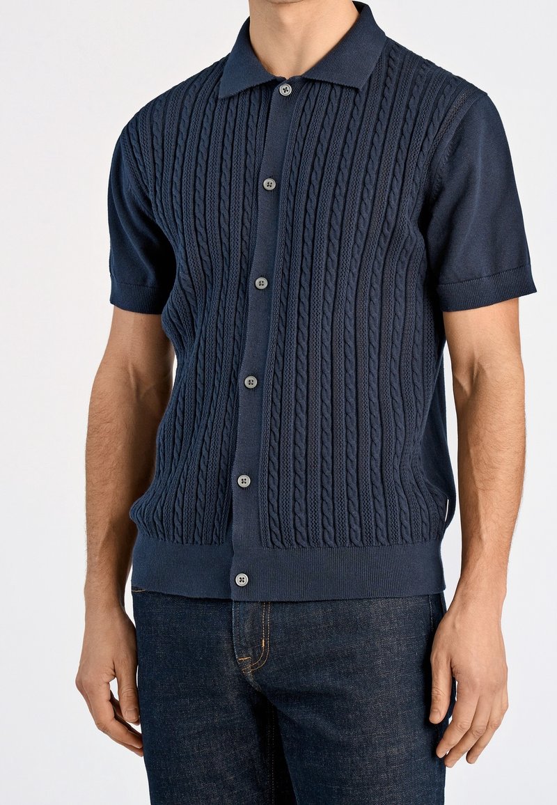 Granatowy, krótki sweter na guziki z teksturowanym wzorem warkocza, pięcioma guzikami z przodu oraz prążkowanymi mankietami i dołem, wykonany z miękkiego materiału.