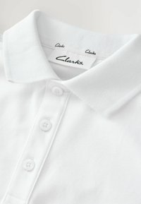 Valge polo särk tekstureeritud kangaga, kolm valget nööpi ja klassikaline krae. Siseetiketil on "Clarks" logo.