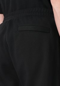 Black sweatpants feature a soft, smooth texture, elastic waistband, and a single back pocket with a rectangular flap.