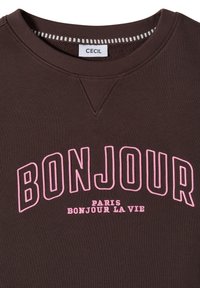 Sweat-shirt marron à col rond avec le texte "BONJOUR" en rose souligné, et la broderie plus petite "PARIS BONJOUR LA VIE" en dessous, étiquette indiquant "CECIL".