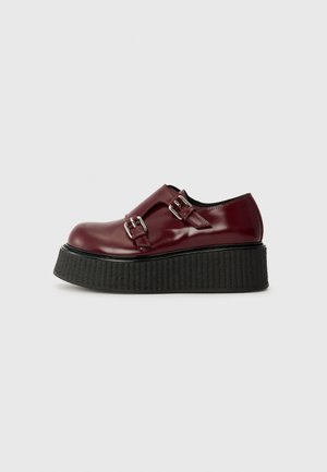 Burgundy patent leather shoes with two silver buckles, high textured black platform sole, and rounded toe design.