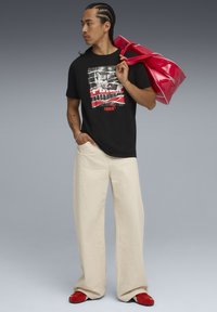 Black graphic T-shirt featuring a red and white design, cream wide-leg pants, red slip-on shoes, and a glossy red duffle bag.