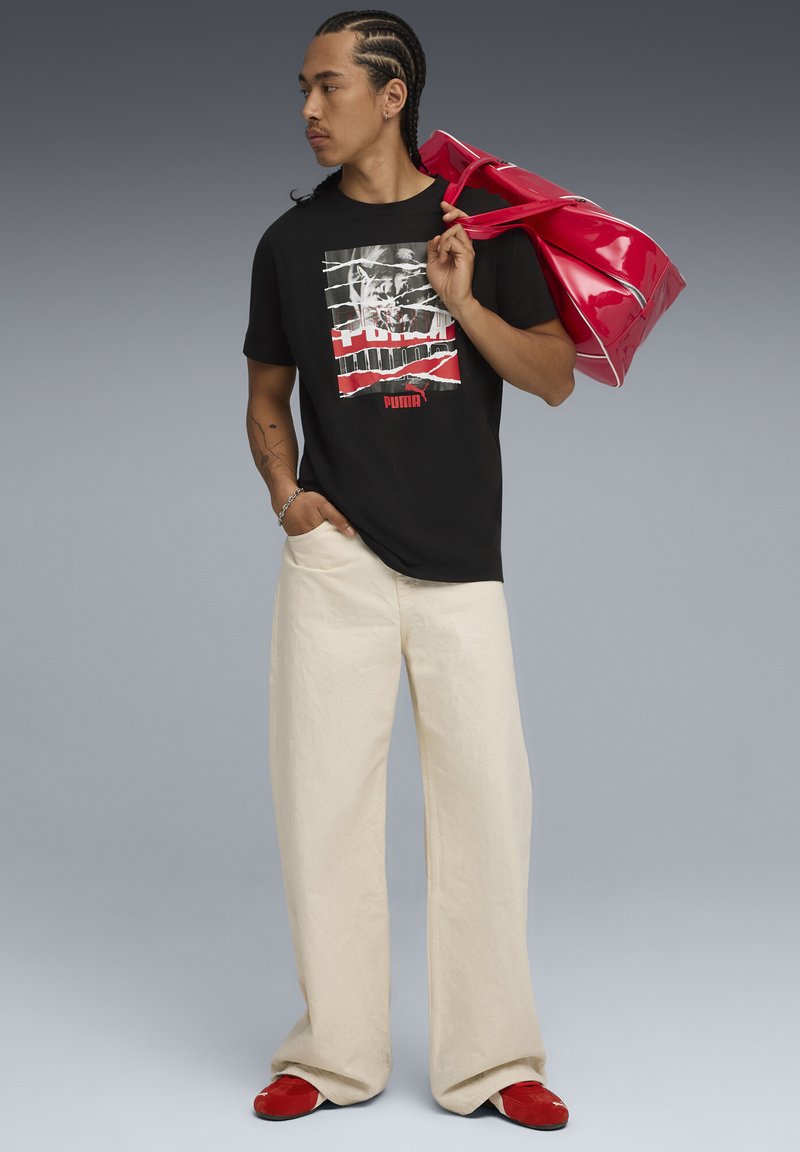 Black graphic T-shirt featuring a red and white design, cream wide-leg pants, red slip-on shoes, and a glossy red duffle bag.