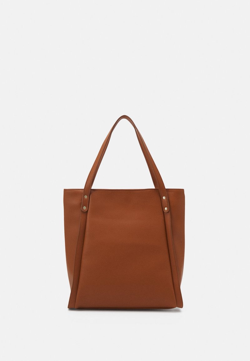 Sac cabas en cuir marron avec deux longues anses et détails minimes de rivets en métal sur un fond uni.