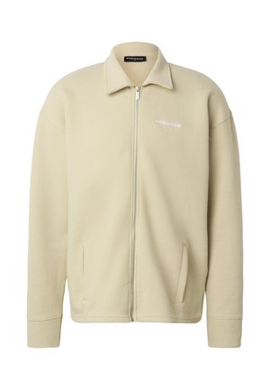 Béžová pletená bunda na zip s límcem, dlouhými rukávy, bočními kapsami a malým bílým logem značky na levé straně hrudi.
