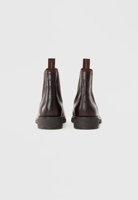 Pair of dark brown leather ankle boots with black soles, viewed from the back against a plain light gray background.