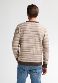 Gestreifter Pullover in Braun und Creme mit geripptem Ausschnitt und Bündchen, aus strukturiertem Strickstoff gefertigt, kombiniert mit hellblauen Jeans.