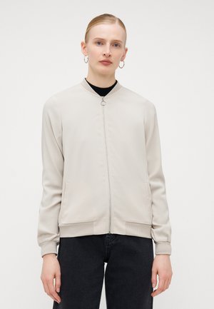 Lyse beige bomberjakke med glidelås foran, ribbede mansjetter og lommer. Glatt tekstur med et minimalistisk design.