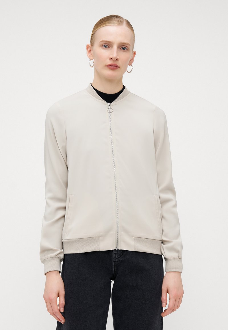 Světle béžová bomber bunda se zipem vpředu, pružnými manžetami a kapsami. Hladká textura s minimalistickým designem.