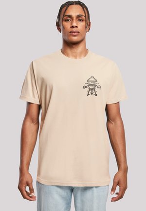 Beige cotton t-shirt featuring a black graphic print of a grill and text "GRILL MASTER DAD" on the left chest. Short sleeves, crew neck design.