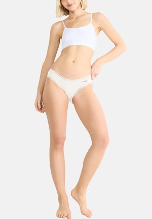 Weißes Unterhemd mit dünnen Trägern, kombiniert mit cremefarbenen Unterhosen mit einem durchbrochenen Saum an den Kanten. Strukturiertes Material, minimalistisches Design.