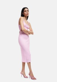 Gebreide roze midi-jurk met een toegesneden silhouette, ronde halslijn en dunne bandjes; gecombineerd met roze sandaaltjes met hoge hakken.
