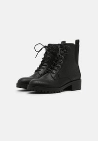 Black ankle boots made of textured material with a lace-up front, round toe, and a chunky heel. Features decorative stitching.