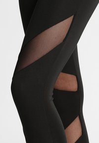 Leggings negros con recortes de malla translúcida en forma de zigzag a lo largo de los lados, que contrastan las texturas de la tela.