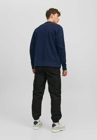 Sweatshirt en col rond bleu marine avec ourlet côtelé, associé à un pantalon cargo noir avec poches latérales et poignets élastiques ; des baskets blanches complètent le look.