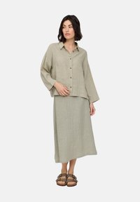 Light green linen shirt and matching skirt set, featuring a collar, button closures, and relaxed fit. Worn with brown slide sandals.