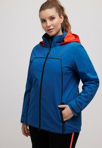 Blauwe waterdichte jas met oranje capuchon, ritssluiting en meerdere zakken. Heeft zwarte accenten en een logo op de borst. Gladde textuur.