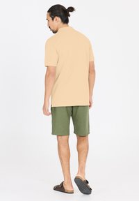 Beige polo-paita, vihreät shortsit ja ruskeat sandaalit. Paidassa on kaulus, ja shortseissa on teksturoitu kangas. Näkymä takaa.