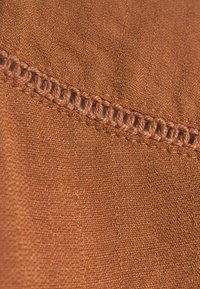 Braun gewebter Stoff mit einer glatten Textur. Verfügt über eine dekorative, gestickte Kante in einem helleren Braun, die einen Kontrast zum Hauptstoff bildet.