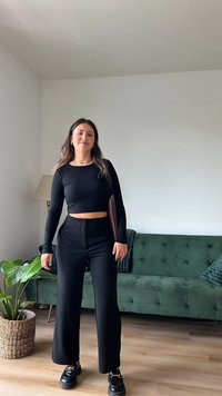 Top preto cropped de mangas longas combinado com calças largas pretas de cintura alta e calçado chunky preto, situado numa sala bem iluminada com detalhes em verde.